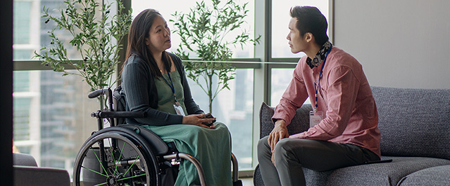 A woman in a wheelchairtalking with a man sitting on a couch.