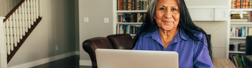 A women in her home, seated at a desk in front of a laptop computer.