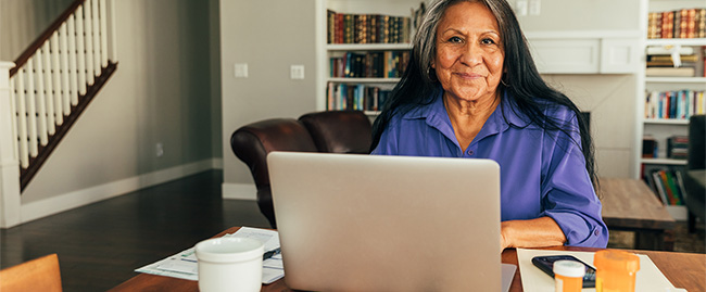 A women in her home, seated at a desk in front of a laptop computer.