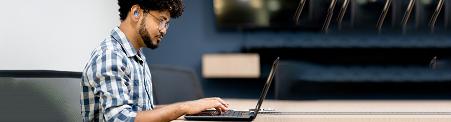 A man with a heading aid sites at a desk using a laptop computer.