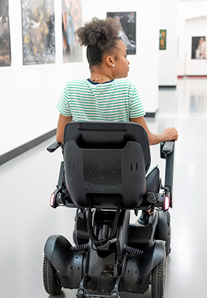 Girl in a wheelchair moving through a large room with photos or paintings displayed on the wall