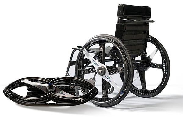 Figure 4: MORPH™ Foldable Wheelchair Wheels: This is an image of a black wheelchair with the Morph wheels attached. A folded Morph Wheel is situated on the ground in front of the wheelchair