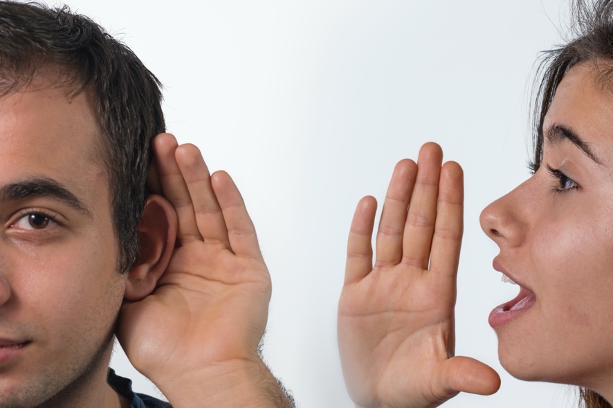 A person with their hand to their ear listening to another person speaking into their ear.